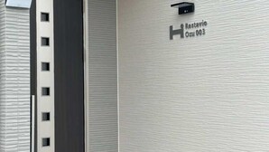 A modern hotel entrance with a textured wall, a door with a vertical handle, and a sign indicating the name and room number. - 10 mins to Kumamoto Airport Premium 4BR Retreat by Restavio (Ozu)