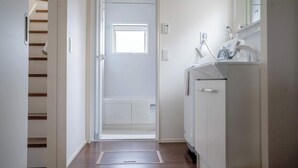 Un pasillo con piso de madera, una puerta blanca que da a una habitación y un armario blanco con un espejo.