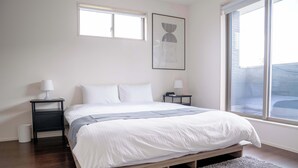 Un dormitorio con una cama, dos mesitas de noche, un ventanal y una obra de arte enmarcada en la pared.