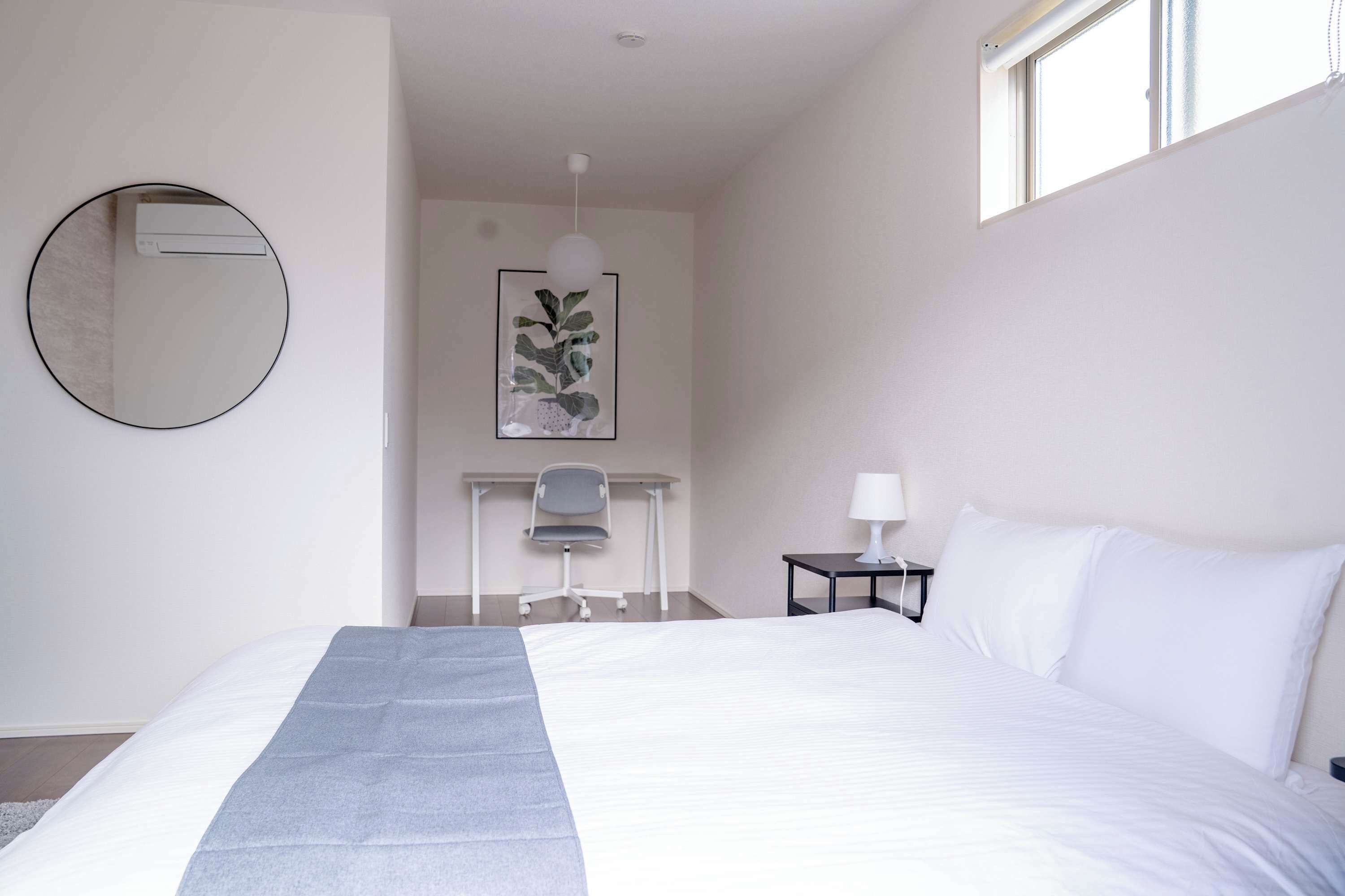 A hotel room with a large bed, a desk with a chair, a small table with a lamp, and a framed artwork on the wall.