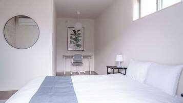 A hotel room with a large bed, a desk with a chair, a small table with a lamp, and a framed artwork on the wall.