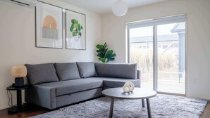 Un saló modern amb un sofà seccional gris, una taula de centre rodona i una finestra gran que ofereix vistes a l'exterior.