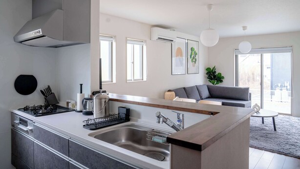 Una cocina moderna con una isla central, electrodomésticos de acero inoxidable y una campana extractora gris. Hay ventanas que ofrecen luz natural y vistas de la ciudad.