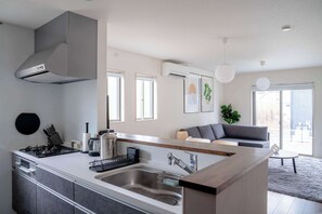 A modern kitchen with a central island, stainless steel appliances, and a grey hood. There are windows providing natural light and a view of the city. - 25 mins to Aso Volcano Serene 4BR House by Restavio (Ozu)