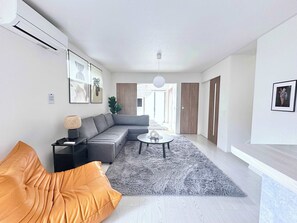 A modern living room with a grey sectional sofa, a round coffee table, and a grey shaggy rug. - Near Airport and Aso Volcano Modern 4BR Residence by Restavio (Ozu)