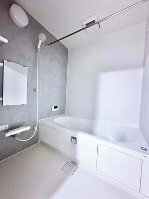 A modern bathroom with a large bathtub, a handheld showerhead, a towel rack, and a wall-mounted mirror. - Near Airport and Aso Volcano Modern 4BR Residence by Restavio (Ozu)