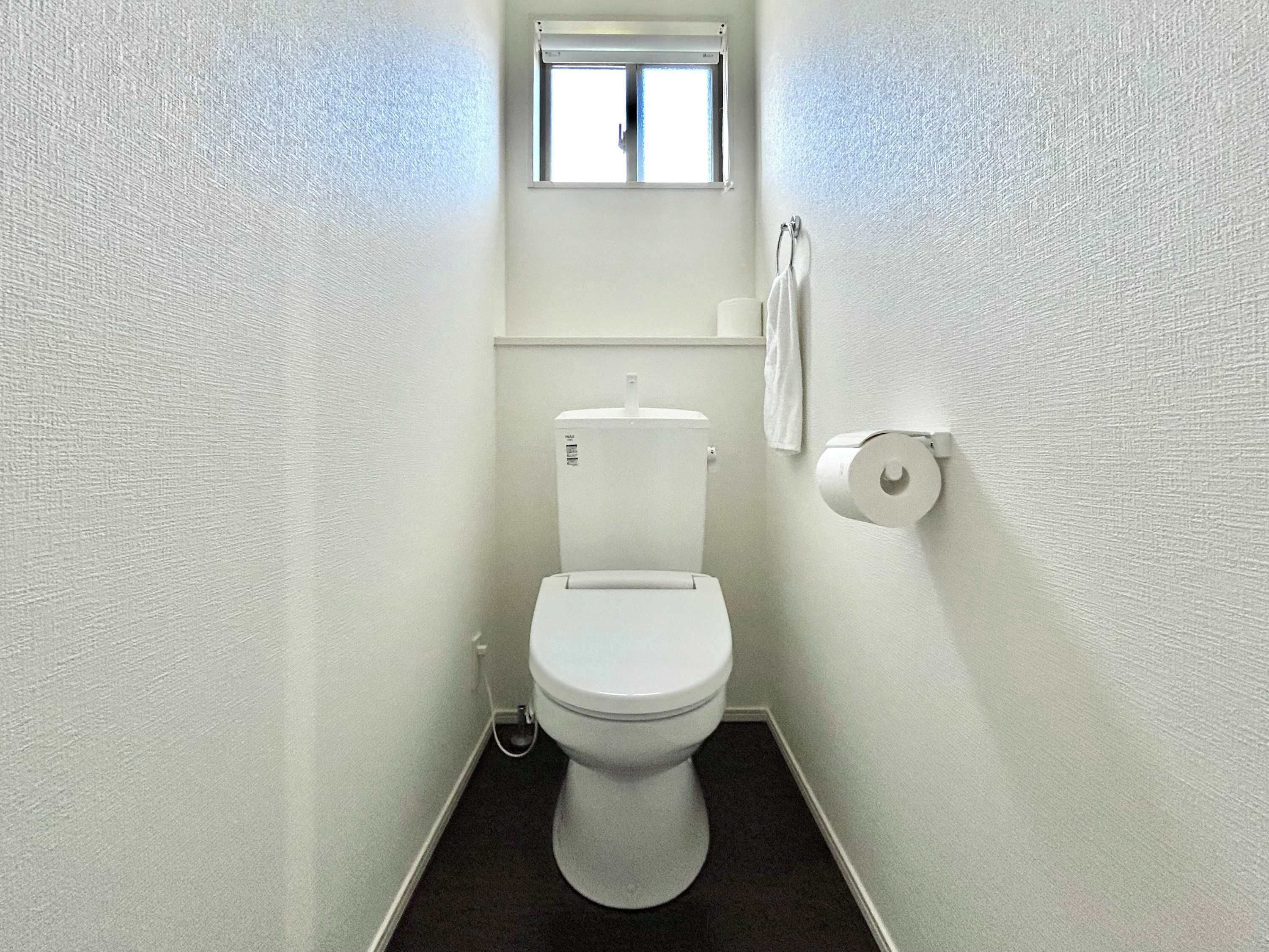 Un baño pequeño y blanco con inodoro, ventana y toallero.
