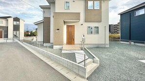 Ein modernes, zweistöckiges Haus mit einer Holztür, einer kleinen Veranda und einem Schotterweg.