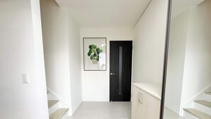 Ein Flur mit hellem Boden, einer dunklen Tür und einem gerahmten Bild einer Pflanze an der Wand.