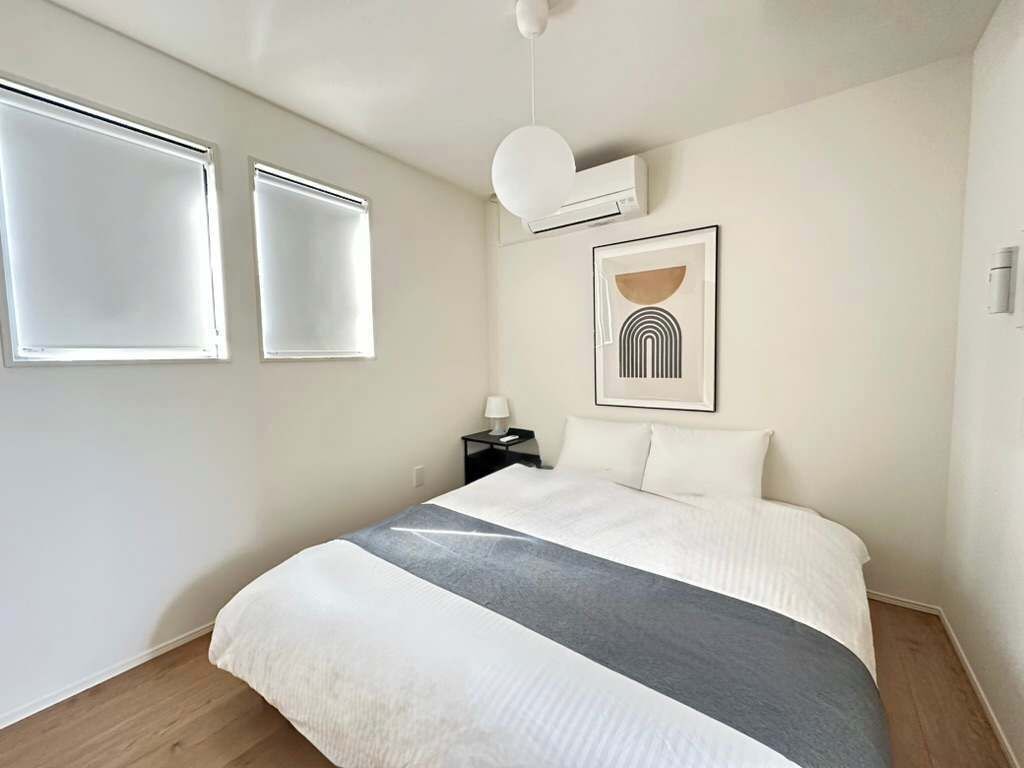 A bedroom with a bed, two bedside tables, a wall-mounted air conditioner, and a framed picture.