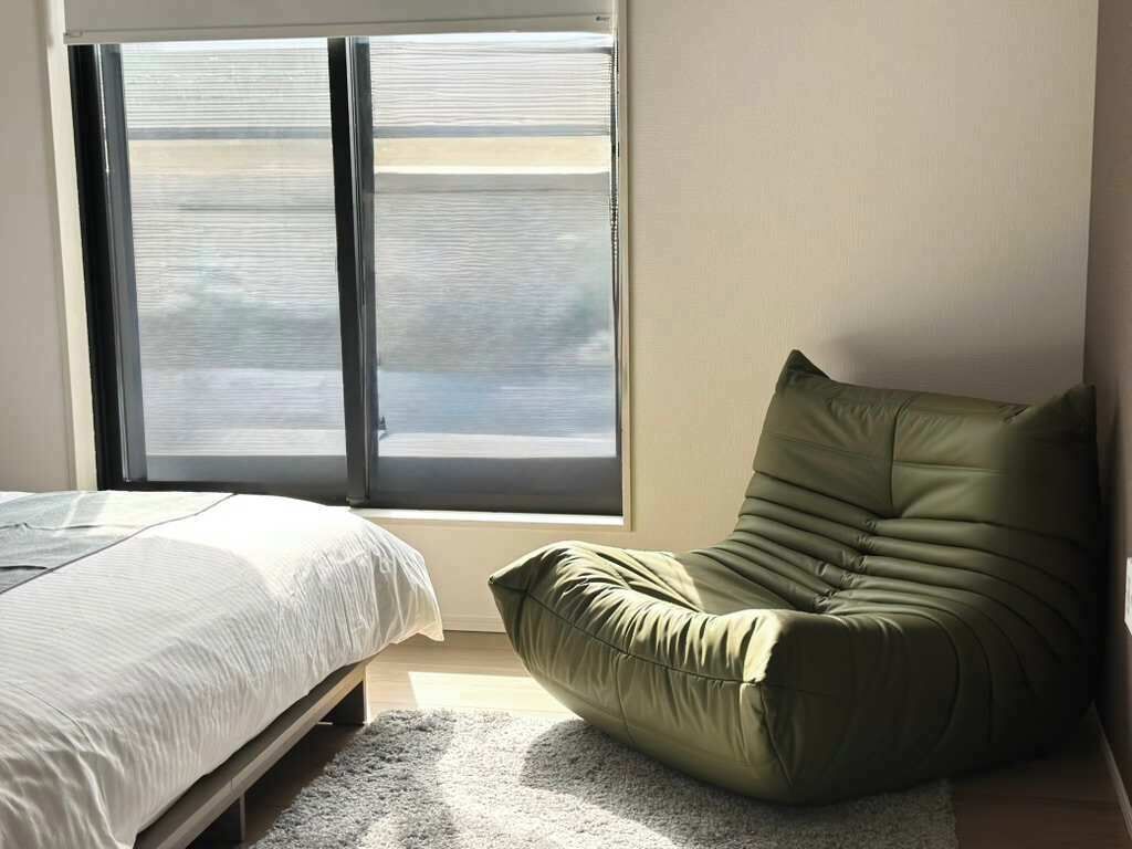 Een slaapkamer met een bed, een groene stoel en een groot raam.