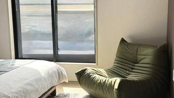 Een slaapkamer met een bed, een groene stoel en een groot raam.