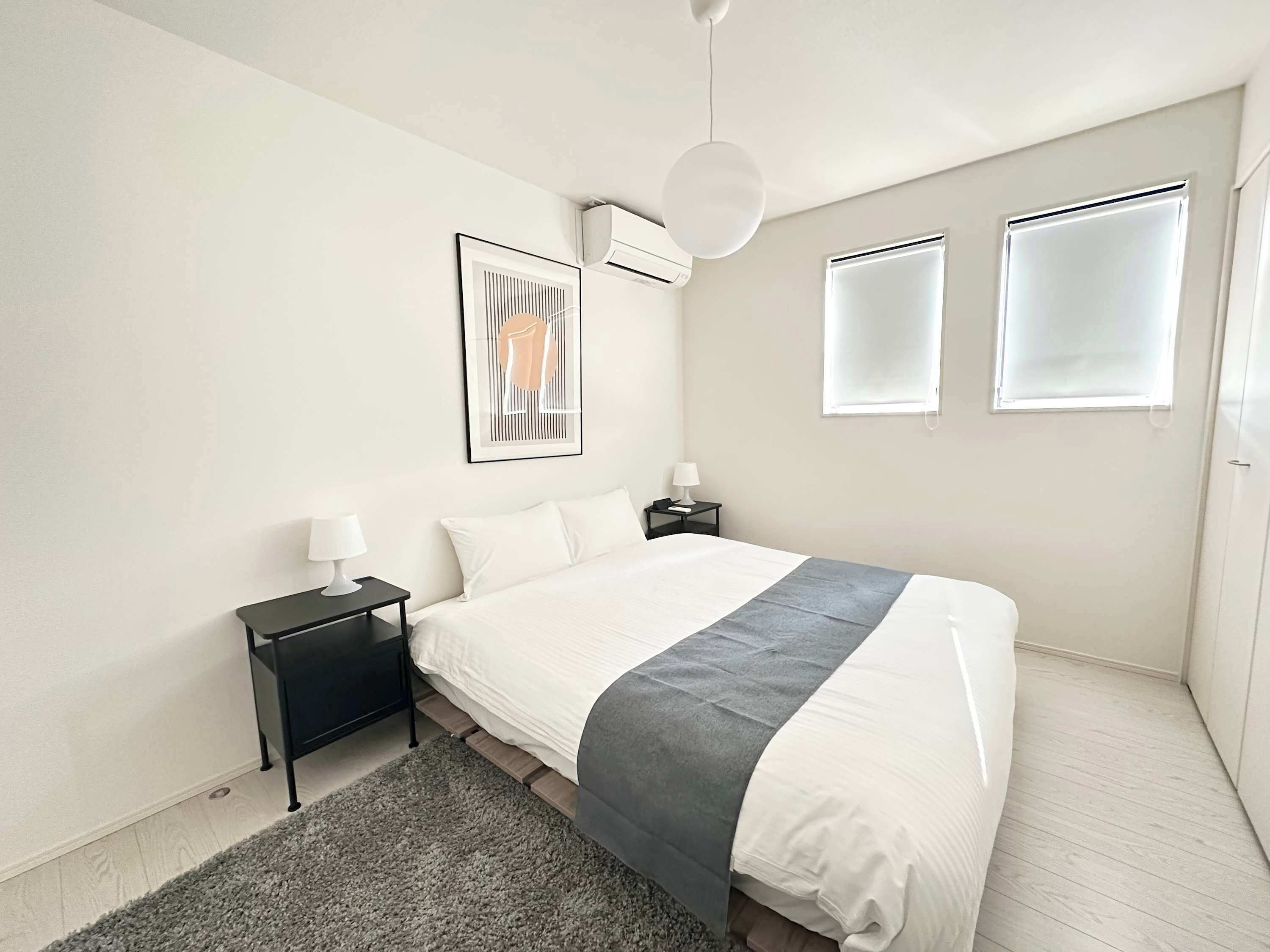 Un dormitorio moderno con una cama grande, una mesita de noche con lámpara, un cuadro enmarcado en la pared y una luz en el techo.