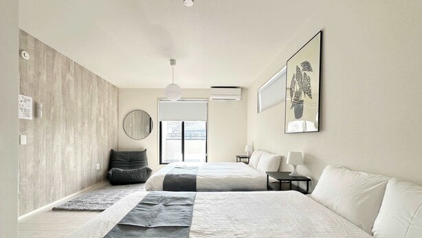 A modern bedroom with two beds, a large mirror, a round mirror, a ceiling light, and a window with blinds. - 10 mins to kumamoto airport Spacious 4BR House by Restavio (Ozu)