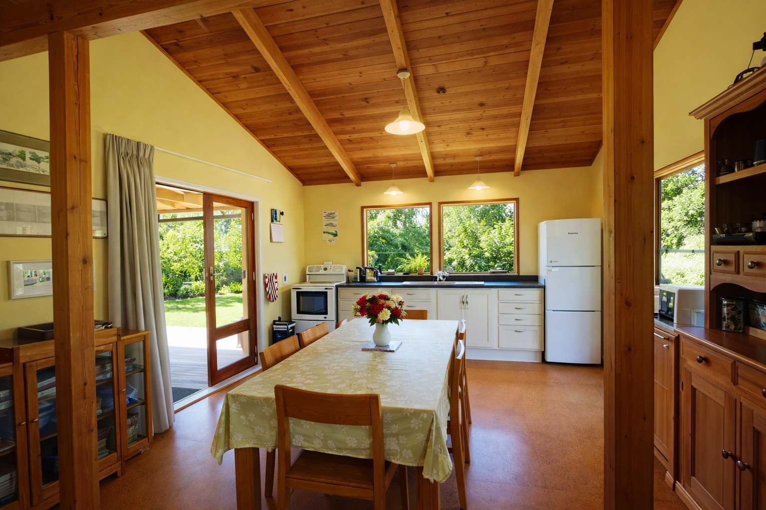 Una cocina acogedora con vigas de madera, una mesa de comedor con sillas, un refrigerador y una ventana con vistas a la vegetación.