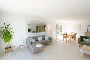 A modern living room with a grey sofa, a dining table with chairs, a large mirror, and a potted plant. - Patons Rock Latitude - Modern Getaway (Patons Rock)