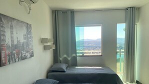 A hotel room with two beds, a large window with a city view, and a painting on the wall. - Complete two-story house in Escarpas do Lago – Comfort and Leisure: Your Dream Retreat (Capitólio)