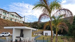 A modern outdoor seating area with white chairs and tables, a grill, and a view of a building in the background. - Complete two-story house in Escarpas do Lago – Comfort and Leisure: Your Dream Retreat (Capitólio)