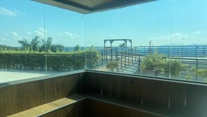 A modern interior with a large glass window offering a view of a coastal area, including a bridge and palm trees. - Complete two-story house in Escarpas do Lago – Comfort and Leisure: Your Dream Retreat (Capitólio)