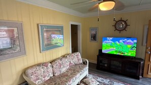 Ein Wohnzimmer mit einem blumigen Sofa, einem Fernseher, einem Deckenventilator und einer Schiffsraddekoration.