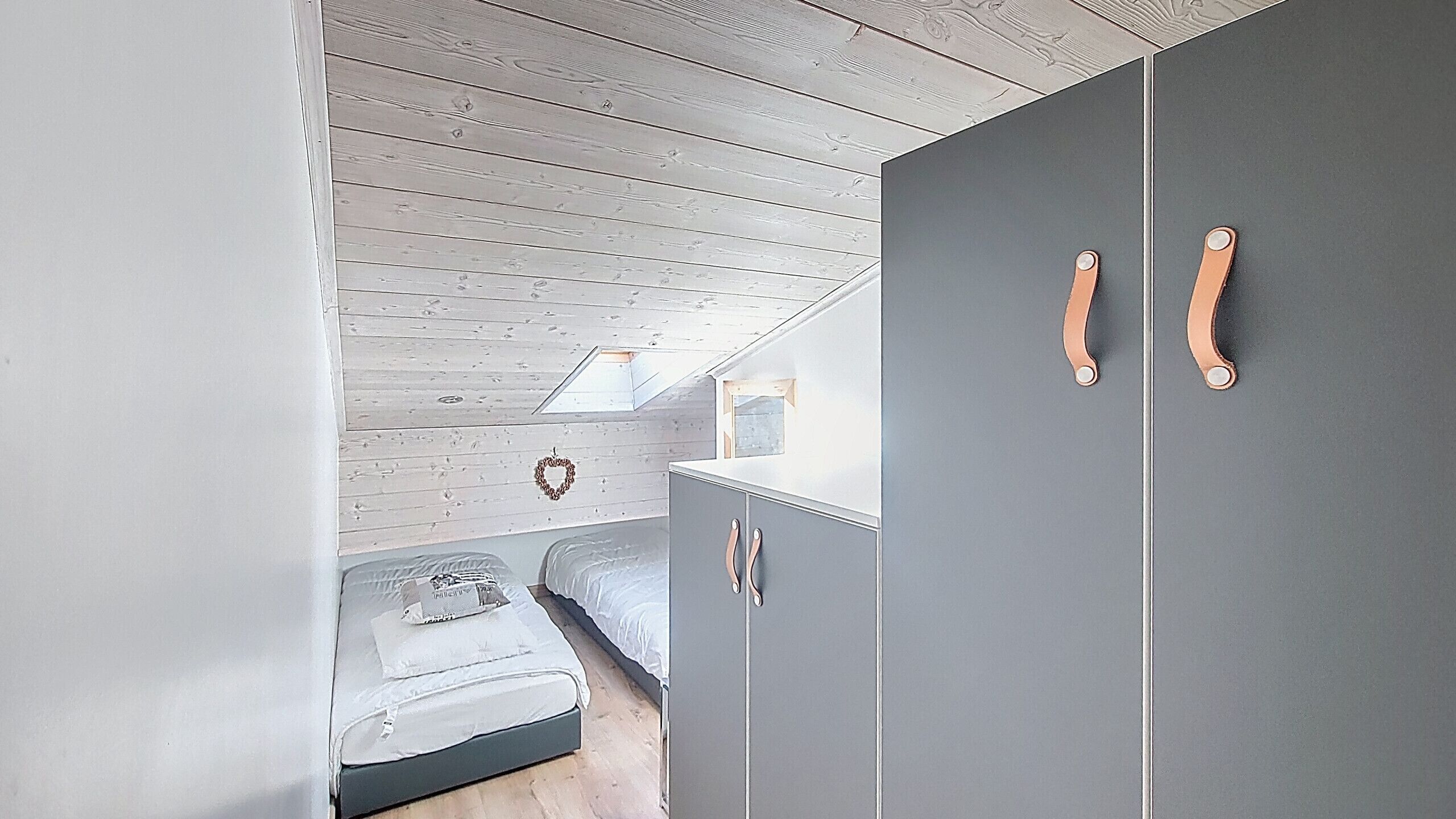 A bedroom with a loft-style ceiling, a bed, a wardrobe, and a small window.