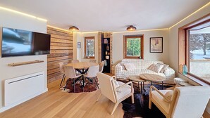 Ett modernt vardagsrum med en TV, en väggpanel i trä, en soffa, stolar och ett matbord.