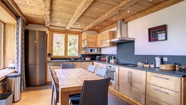 Eine moderne Küche mit Holzausbau, einem Edelstahlkühlschrank und einem Essbereich mit Holztisch und Stühlen.