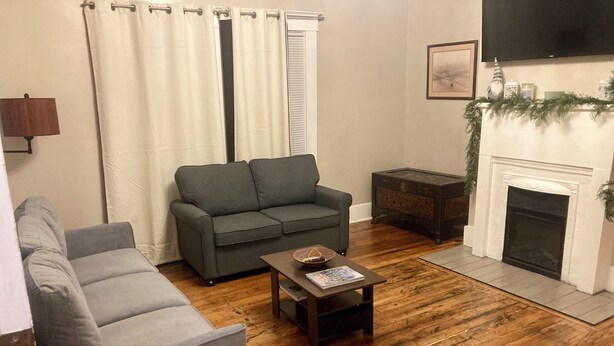 Una sala de estar con un sofá gris, una mesa de centro con una revista, una chimenea y un televisor montado en la pared.