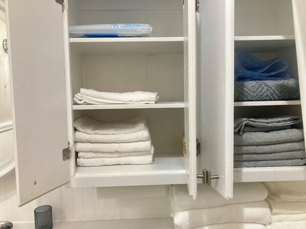 A white storage cabinet with multiple shelves, some holding folded towels and others with plastic bags. - The Blue Note-Duplex
Historic District (Memphis)