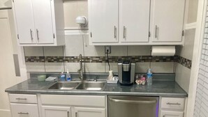 Una cocina con gabinetes blancos, un lavamanos de acero inoxidable, una cafetera y un lavavajillas.