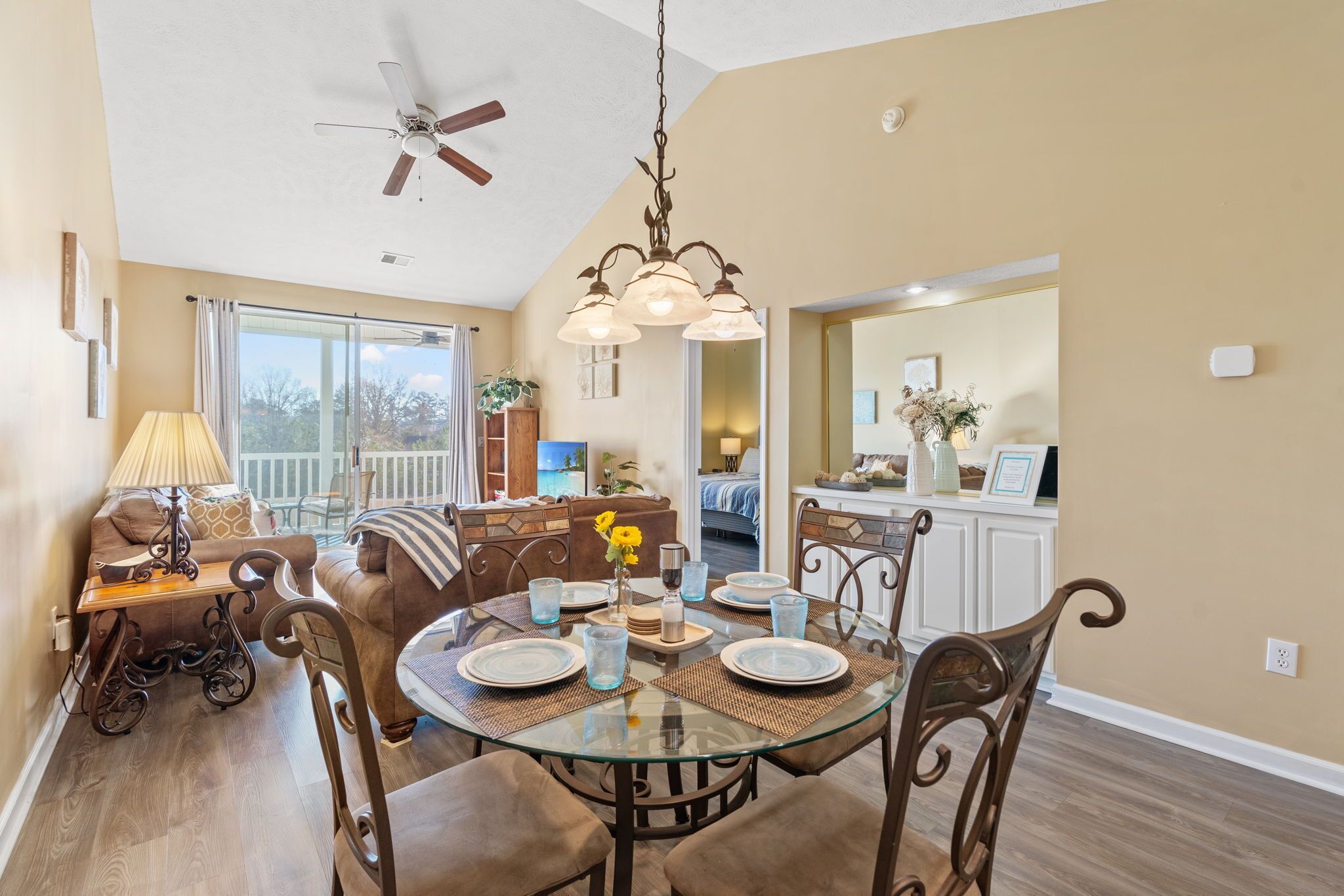 A dining area with a glass table, brown chairs, and a chandelier.
