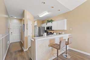 A modern kitchen with white cabinets, stainless steel appliances, and a bar area with two stools. - River Oaks Condo near beach & golf. Pool, tennis & free parking (Myrtle Beach)