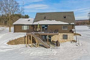 A log cabin with a stone foundation, a covered deck, and a staircase leading to a second level. - Game Room Log Cabin Near Dells Hot Tub (Lyndon Station)