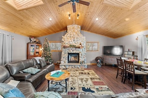 A cozy living room with a stone fireplace, leather sofa, and a dining area. - Game Room Log Cabin Near Dells Hot Tub (Lyndon Station)