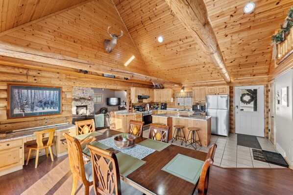Interior de una cabaña de madera con comedor, cocina y chimenea.