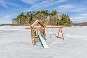 A wooden swing set with a slide in a snowy field.