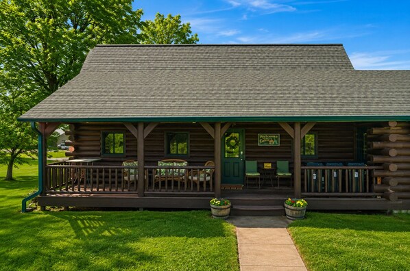 A log cabin with a porch, a welcome sign, and two potted plants.