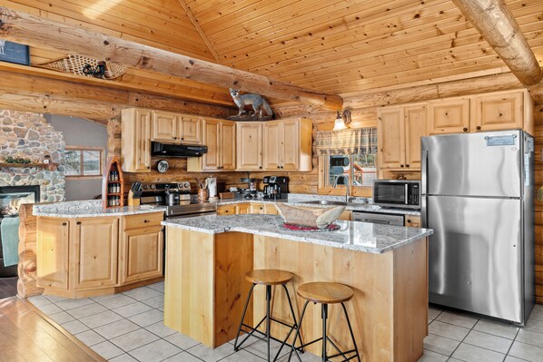 Una cocina amplia con armarios de madera, una isla grande con taburetes, un refrigerador de acero inoxidable y una chimenea de piedra.