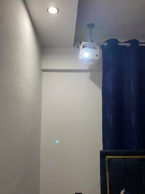 Ein Zimmer mit Deckenlampe, einem an der Wand befestigten Projektor und einem dunklen Vorhang.