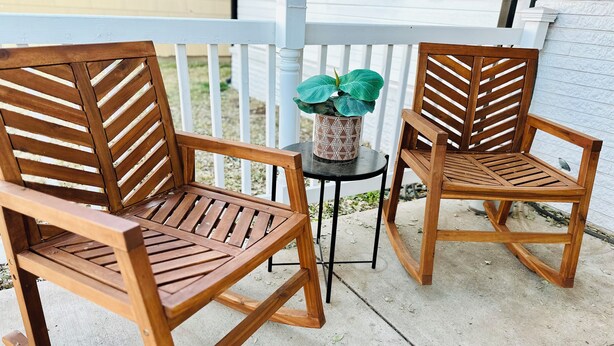 Deux chaises en bois, dotées d’assises et de dossiers à lattes, sont placées sur une terrasse en béton, avec une balustrade blanche en arrière-plan.