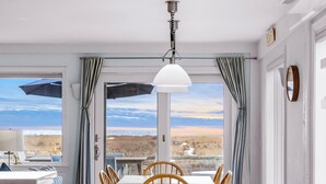 Ein Essbereich mit Tisch und Stühlen, Blick auf den Strand und einer Deckenleuchte.