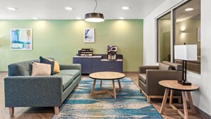 A modern living room with a sofa, a round coffee table, a lamp, and artwork on the walls. - Woodspring Suites Lancaster North (Lancaster)