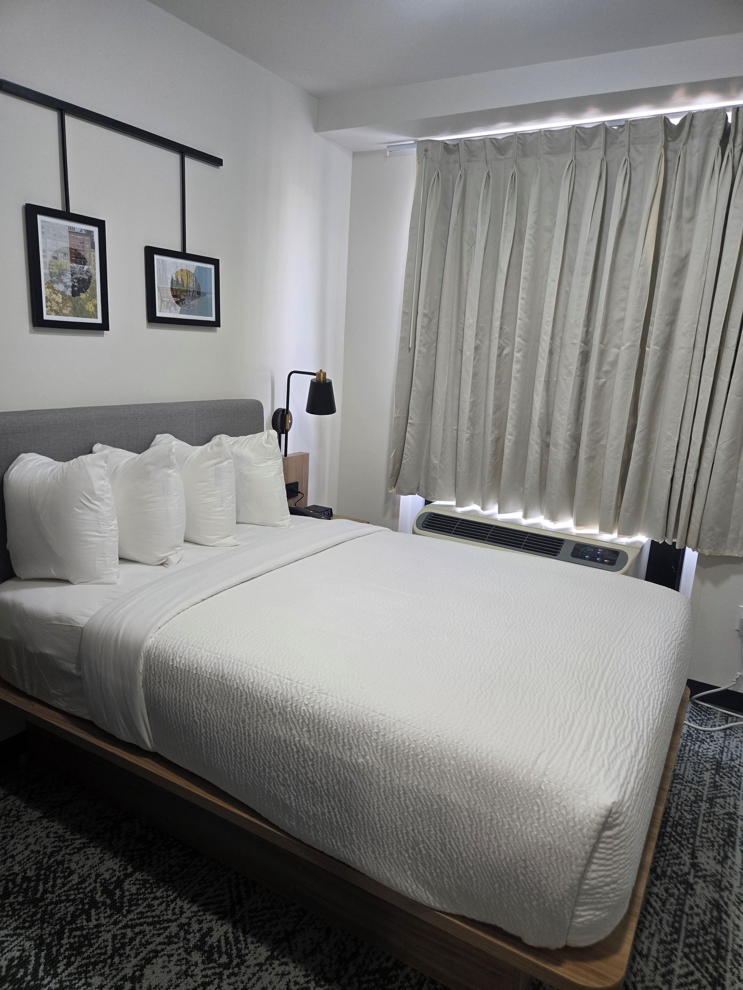 A neatly made bed with white bedding, a bedside lamp, and two framed pictures on the wall.