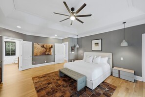 A modern bedroom with a large bed, a ceiling fan, and a view of a garden through a door. - Spacious Lake Norman Home • Hot Tub + Firepit + Deck | Sleeps 22 | Lion Manor (Denver)