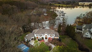A large, two-story house with a spacious front yard, a swimming pool, and a dock extending into a lake. - Lake Norman Estate • Hot Tub + Fire Pit + Movie Theater | Lion Manor (Denver)