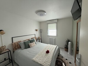 A bedroom with a bed, a bedside table, a lamp, a radiator, a window, and a TV mounted on the wall.
