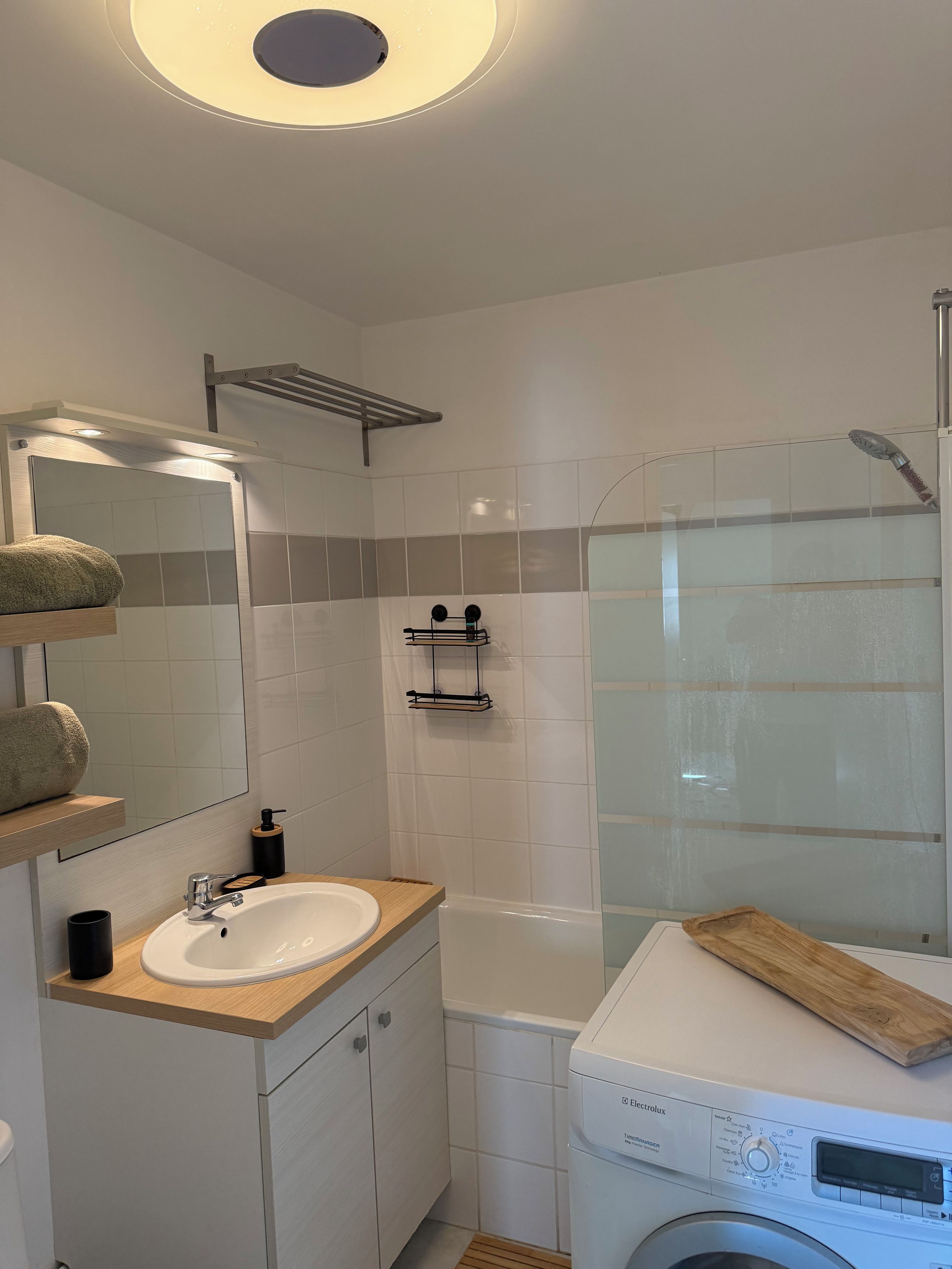 Une salle de bain moderne équipée d’un lavabo, d’un miroir, d’un porte-serviettes et d’un lave-linge.
