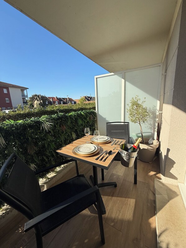 Un espace extérieur aménagé pour prendre les repas, avec une table dressée pour deux personnes, une chaise et un pot de fleurs.