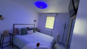 Ein Schlafzimmer mit einem Bett, Nachttischen, einer Lampe, einem Fenster mit Jalousien und einem Fernseher an der Wand.