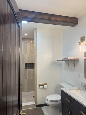 Un baño moderno con lavamanos de mármol, inodoro y zona de ducha.